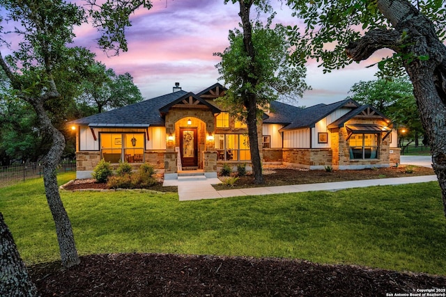 view of front of house featuring a front yard, stone siding, board and batten siding, and fence