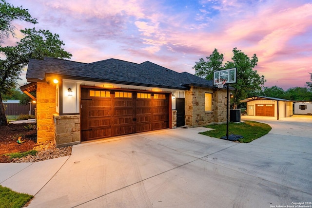 view of front facade featuring driveway, stone siding, an attached garage, and roof with shingles