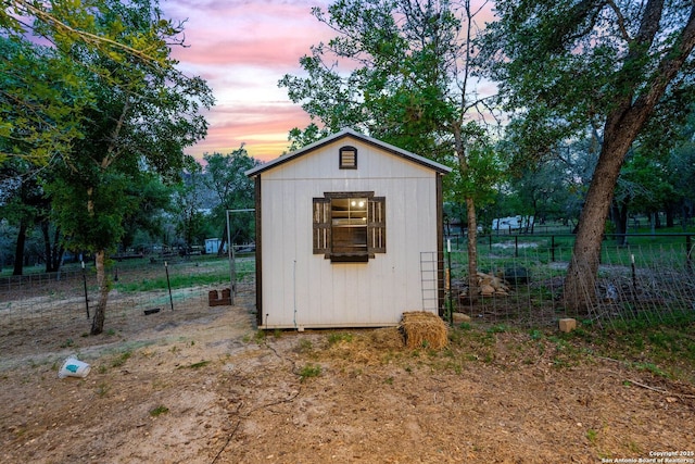 outdoor structure at dusk with fence, a storage unit, and an outbuilding