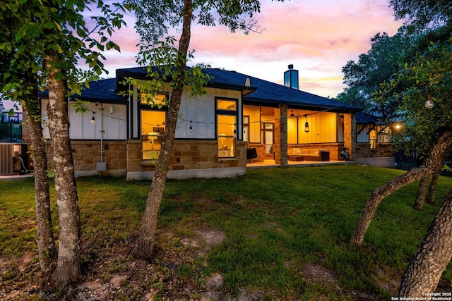 exterior space featuring a yard, a chimney, stone siding, board and batten siding, and roof with shingles