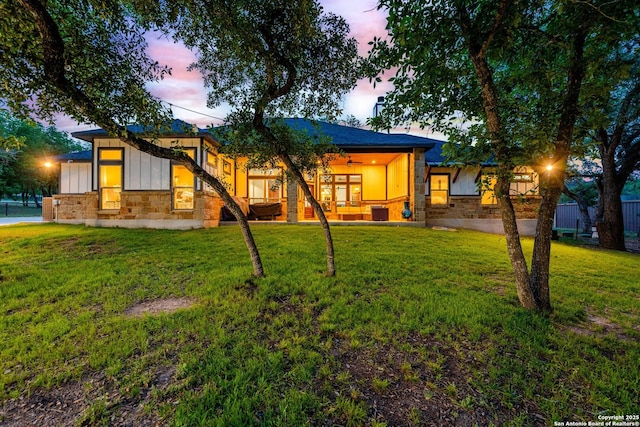 back of house at dusk with a lawn, board and batten siding, and stone siding