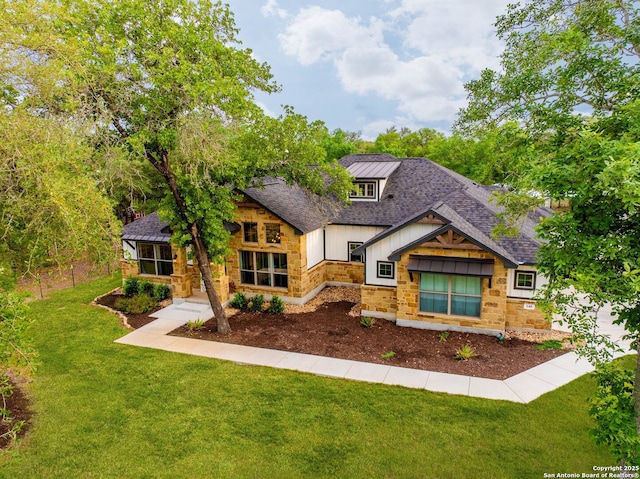 view of front facade with a shingled roof, a front lawn, and stone siding