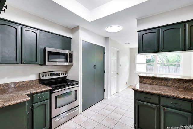 kitchen featuring dark countertops, light tile patterned flooring, green cabinets, and stainless steel appliances