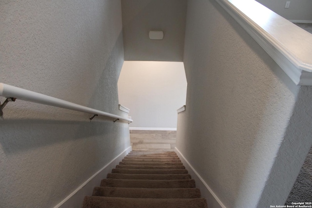 staircase featuring a textured wall and baseboards