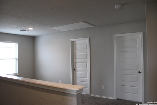 empty room featuring attic access, a textured ceiling, and dark colored carpet