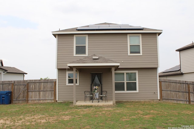 rear view of property with a patio, a fenced backyard, solar panels, and a lawn