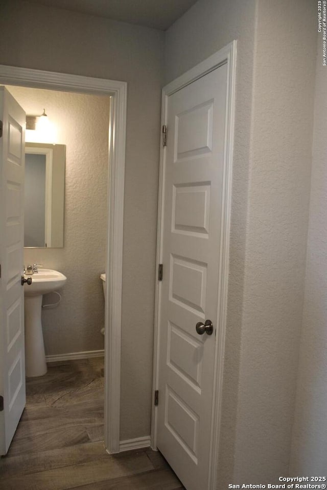 half bath with a sink, wood finished floors, and baseboards