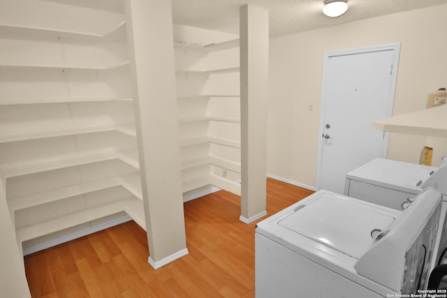 washroom featuring light wood finished floors, a textured ceiling, washing machine and clothes dryer, and laundry area