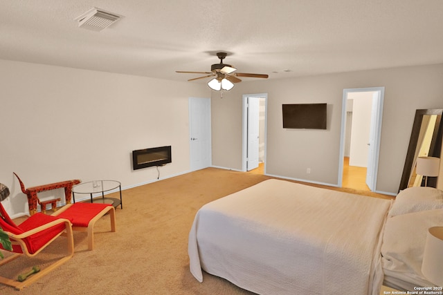 carpeted bedroom with a glass covered fireplace, visible vents, ceiling fan, and baseboards