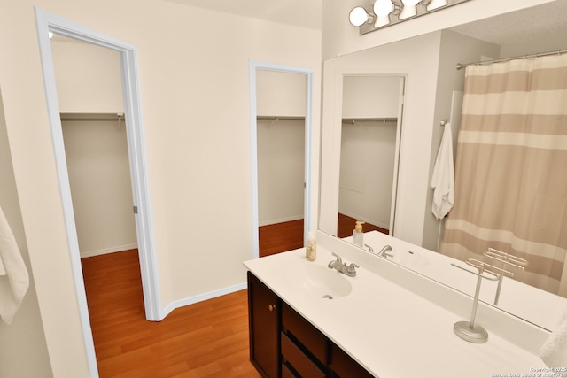 bathroom with vanity, a shower with shower curtain, baseboards, wood finished floors, and a spacious closet