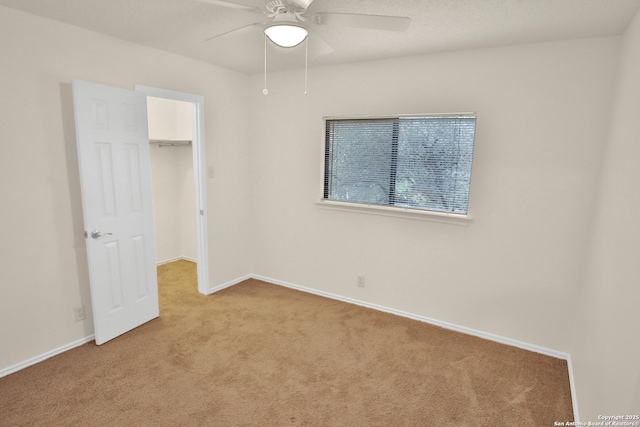 unfurnished bedroom with a closet, a ceiling fan, a walk in closet, baseboards, and carpet floors