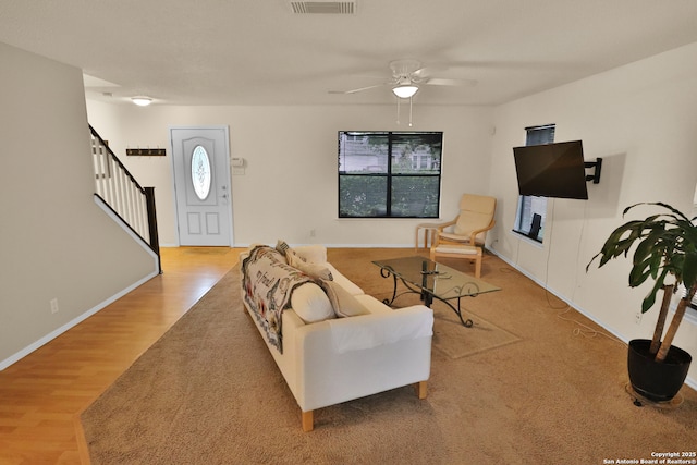 living area with stairway, wood finished floors, a healthy amount of sunlight, and ceiling fan