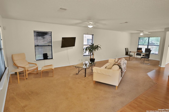 carpeted living area with wood finished floors, a ceiling fan, visible vents, and baseboards
