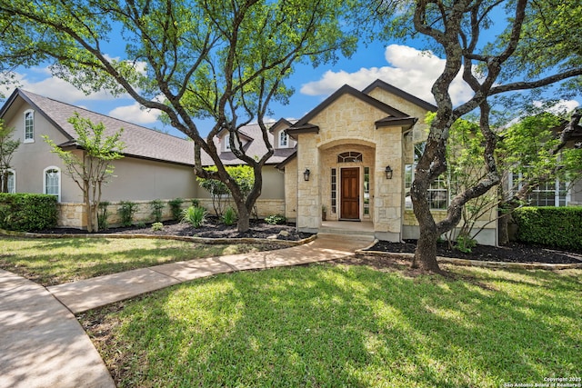 view of front of house featuring stucco siding, roof with shingles, a front lawn, and stone siding