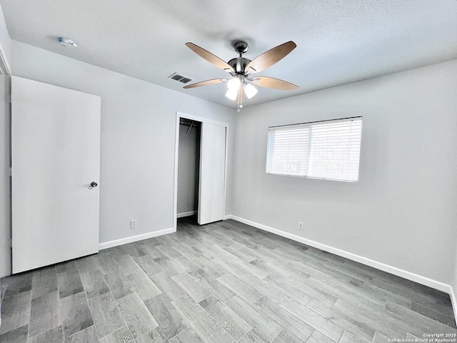 unfurnished bedroom featuring wood finished floors, visible vents, a closet, and baseboards