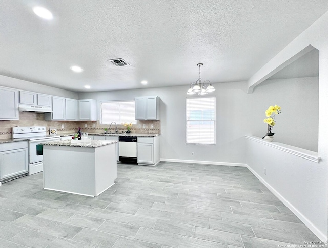 kitchen featuring a chandelier, under cabinet range hood, tasteful backsplash, visible vents, and white appliances