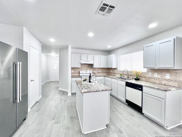kitchen with a sink, under cabinet range hood, a center island, visible vents, and white appliances
