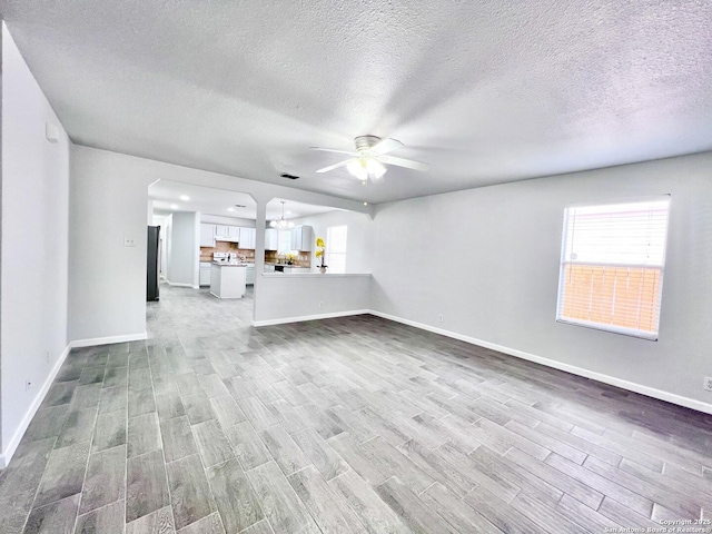 unfurnished living room featuring wood finished floors, plenty of natural light, ceiling fan, baseboards, and a textured ceiling