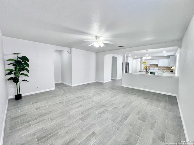 unfurnished living room with arched walkways, baseboards, light wood-style flooring, and ceiling fan with notable chandelier