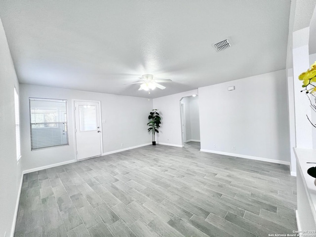 interior space featuring wood finished floors, arched walkways, baseboards, visible vents, and a ceiling fan