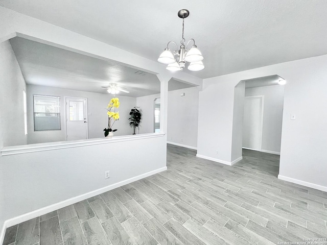 spare room with wood finished floors, ceiling fan with notable chandelier, and baseboards