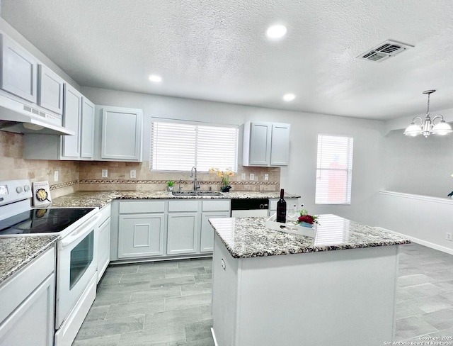 kitchen featuring a sink, under cabinet range hood, visible vents, light stone counters, and white range with electric cooktop
