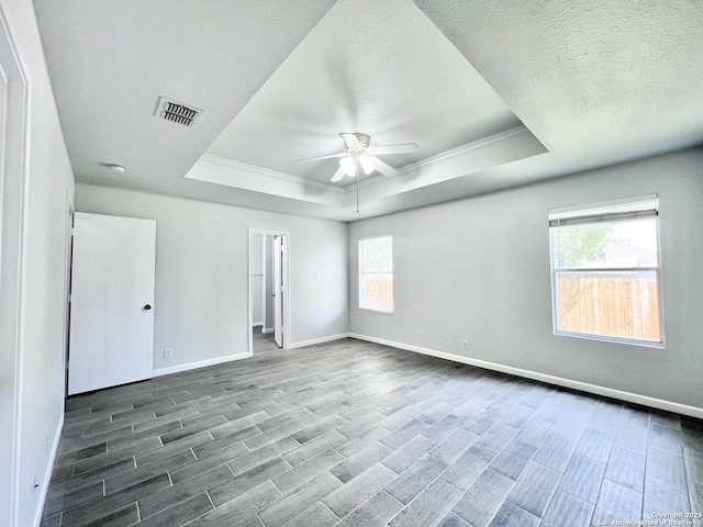 unfurnished bedroom with visible vents, a tray ceiling, baseboards, wood finish floors, and multiple windows