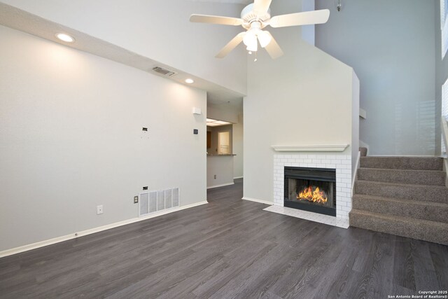 unfurnished living room with ceiling fan, dark wood-style flooring, a fireplace, visible vents, and a towering ceiling