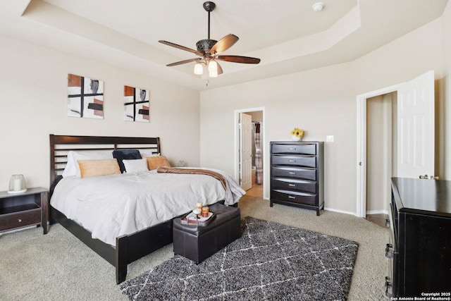 carpeted bedroom featuring baseboards, a raised ceiling, ceiling fan, and ensuite bath