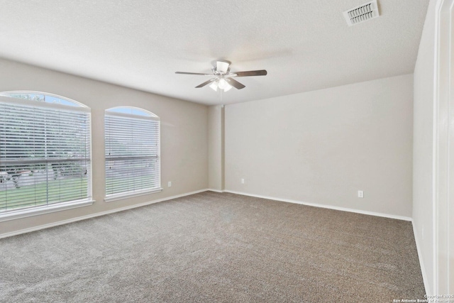carpeted empty room featuring a ceiling fan, visible vents, a textured ceiling, and baseboards