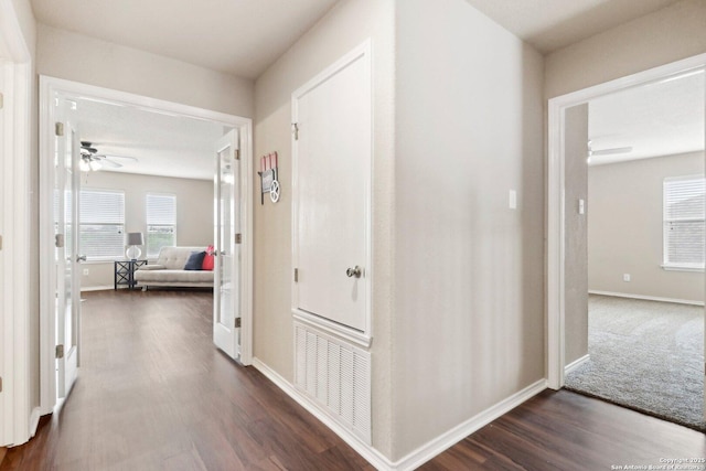 corridor featuring visible vents, dark wood-style flooring, and baseboards