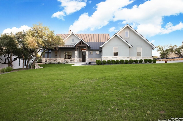 modern farmhouse featuring stone siding, a standing seam roof, metal roof, a chimney, and a front lawn