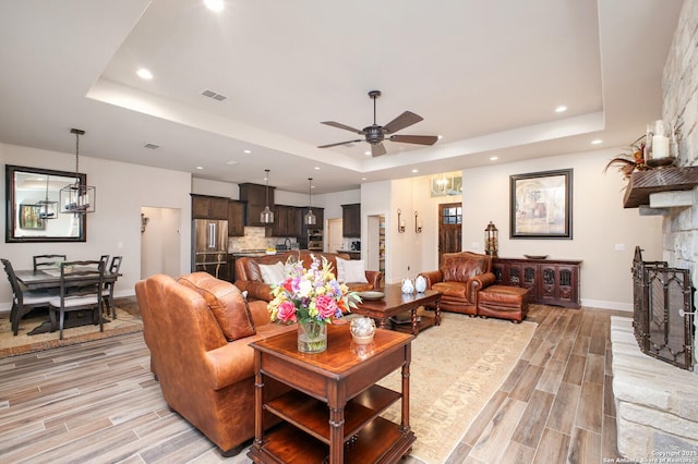 living area with baseboards, visible vents, ceiling fan with notable chandelier, and a tray ceiling