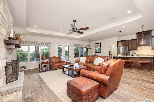 living room featuring recessed lighting, ceiling fan, light wood finished floors, visible vents, and a tray ceiling
