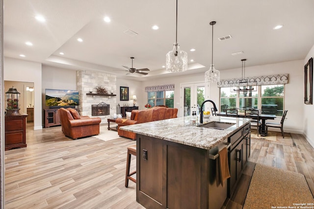 kitchen with a sink, ceiling fan, light wood-type flooring, a stone fireplace, and visible vents