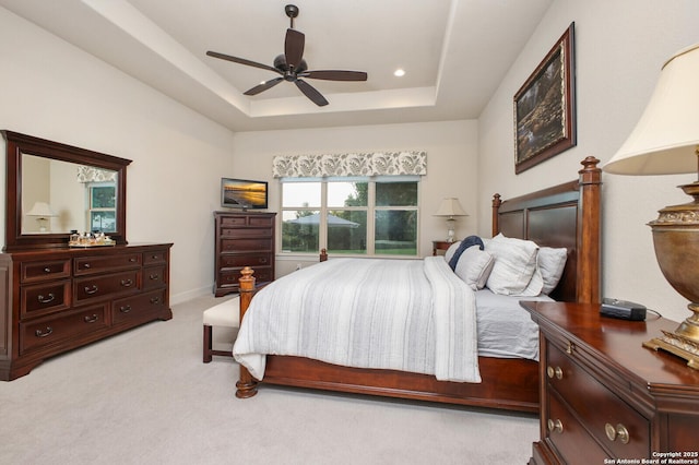 bedroom with a raised ceiling, a ceiling fan, and light colored carpet