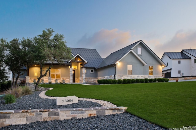 modern farmhouse style home with stone siding, a standing seam roof, metal roof, stucco siding, and a yard