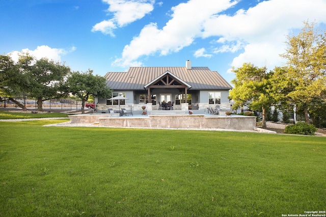 back of property with a patio, a chimney, a standing seam roof, metal roof, and a yard