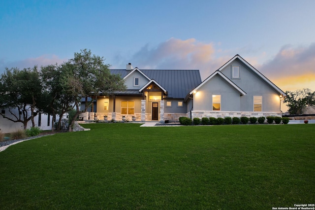 modern farmhouse with a lawn, a standing seam roof, metal roof, and stone siding