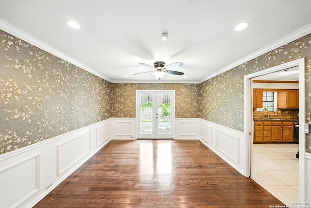 empty room featuring a wainscoted wall, a ceiling fan, wallpapered walls, and french doors