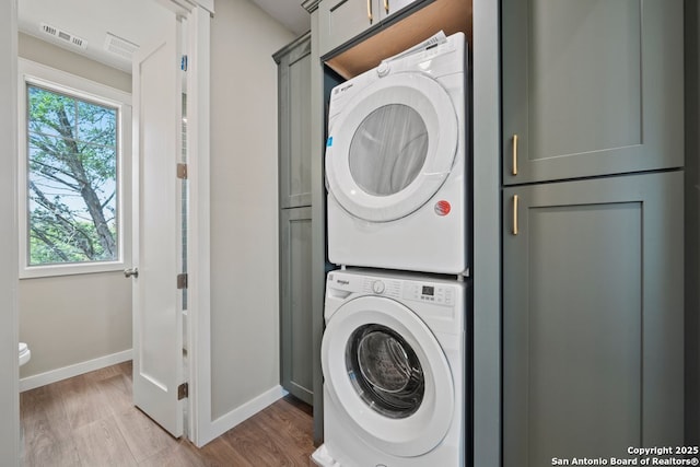washroom with cabinet space, stacked washer and clothes dryer, wood finished floors, and baseboards