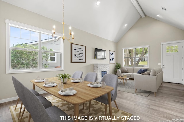 dining area featuring visible vents, light wood-style floors, a fireplace, beam ceiling, and high vaulted ceiling