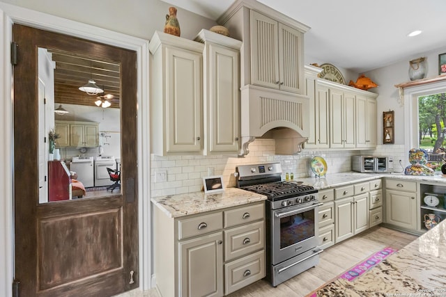 kitchen with cream cabinetry, washer and dryer, stainless steel range with gas stovetop, and tasteful backsplash