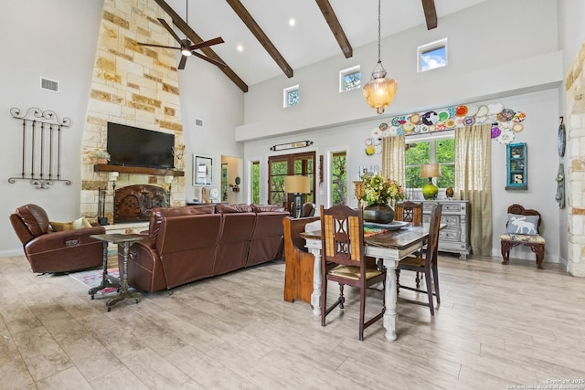 living area featuring a stone fireplace, beam ceiling, visible vents, a ceiling fan, and high vaulted ceiling