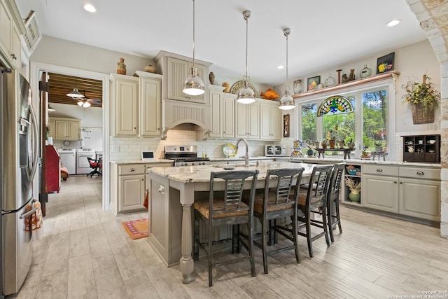 kitchen with appliances with stainless steel finishes, a kitchen island with sink, decorative backsplash, and washing machine and dryer