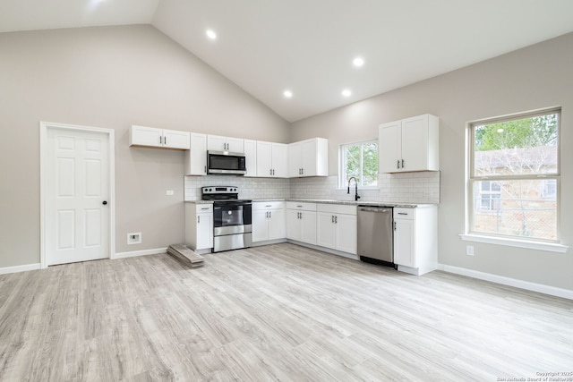 908 Plum, Floresville, TX 78114 - kitchen with white cabinetry, decorative backsplash, a sink, appliances with stainless steel finishes, and light wood-type flooring