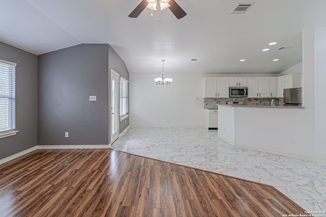 unfurnished living room with visible vents, vaulted ceiling, wood finished floors, and ceiling fan with notable chandelier