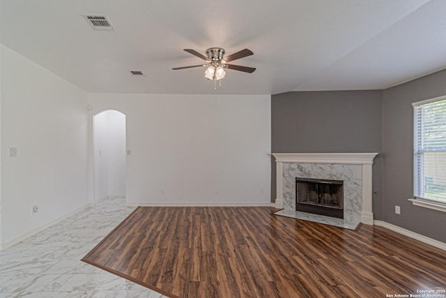unfurnished living room featuring visible vents, arched walkways, ceiling fan, and a high end fireplace