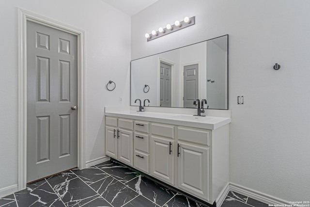 bathroom with baseboards, marble finish floor, double vanity, and a sink