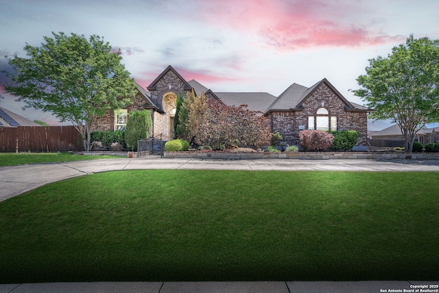 view of front of property featuring fence, a yard, and brick siding